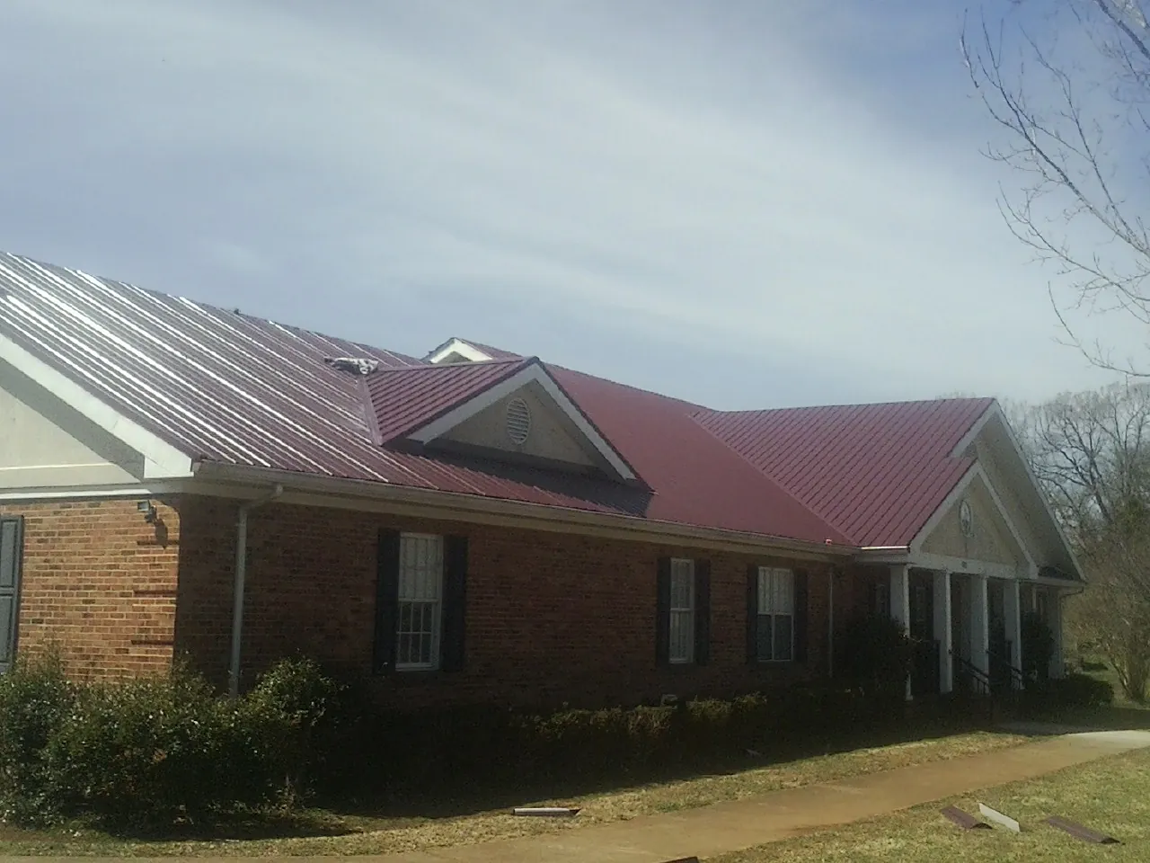 Red metal roof with gabled entries on a long brick building, from a Hail Damage Roof Repair job in Campbell Hall