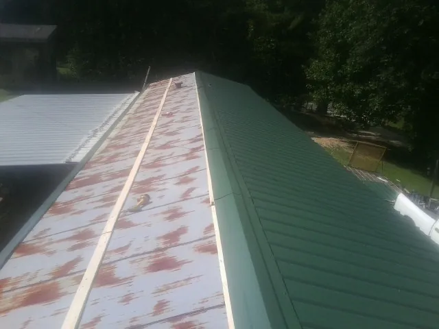 Old rusted panels beside newly installed green metal roofing — Wind Damage Roof Repair by Roofing Brothers in Campbell Hall