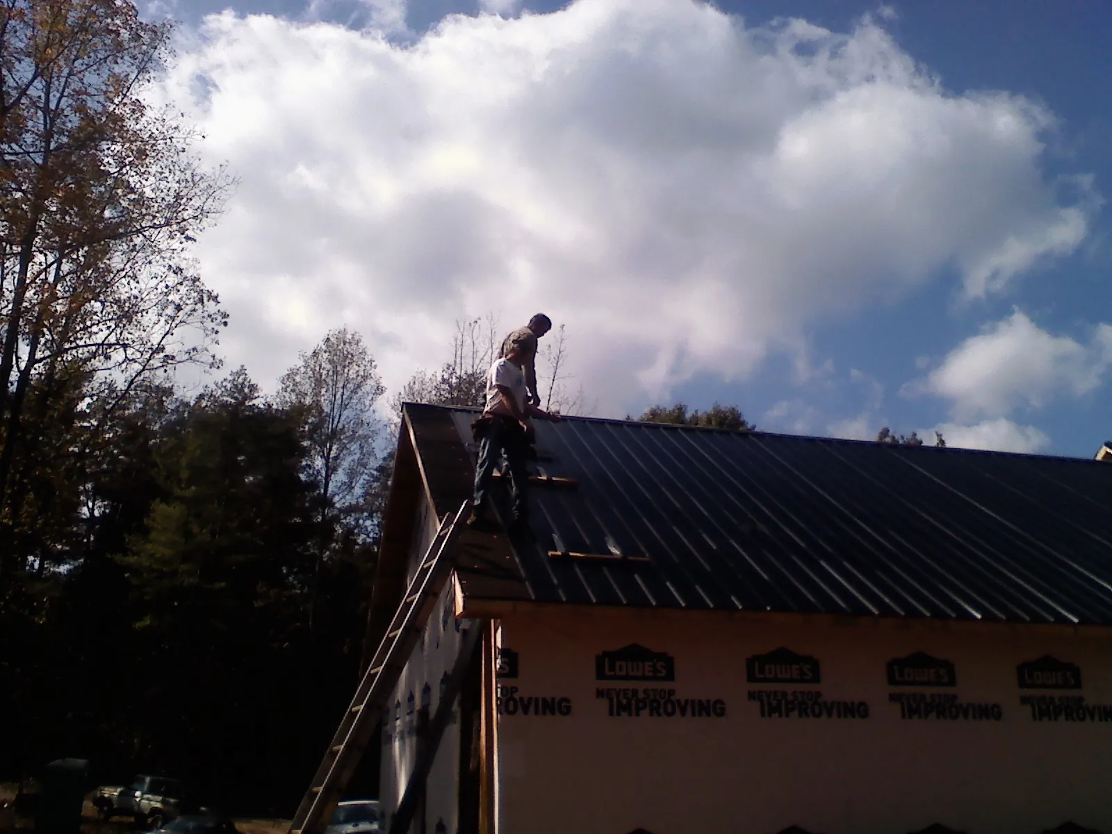 Roofer fastening dark metal panels high against a cloudy sky, from a Roof Inspection job in Campbell Hall