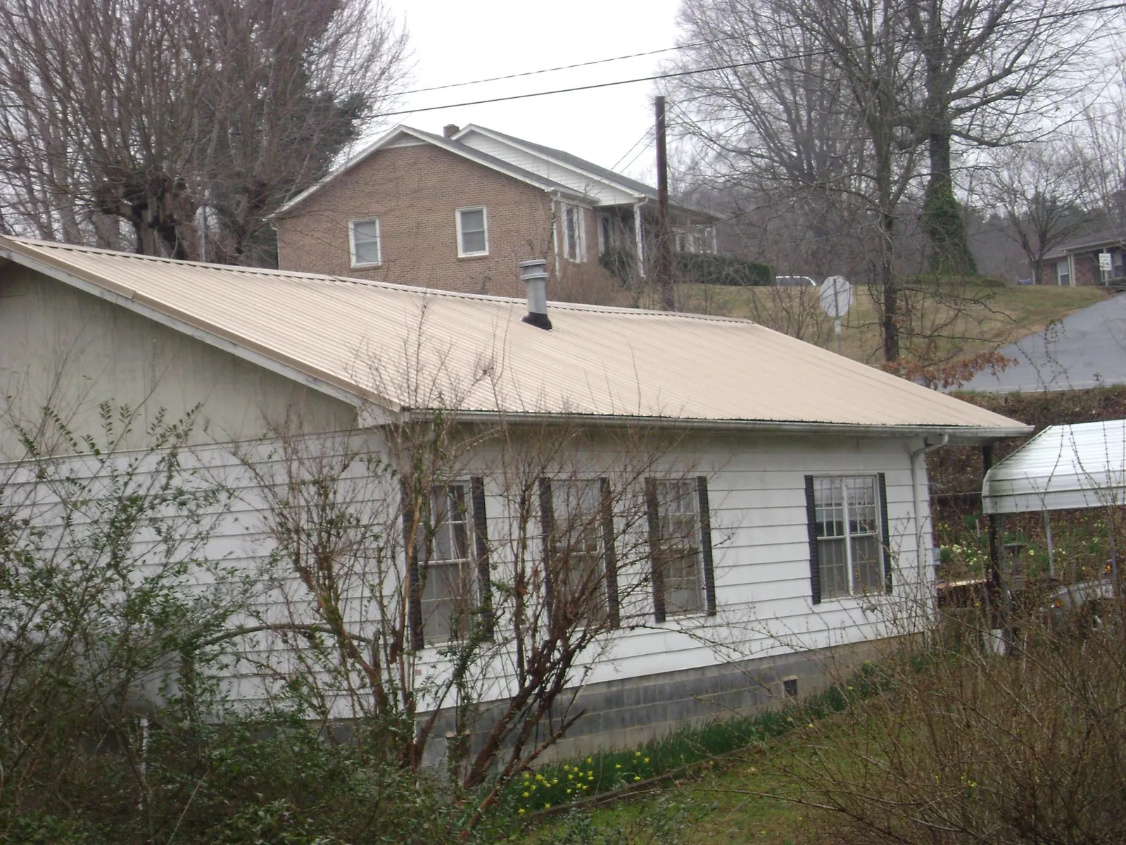 Tan metal roof on a white sided house set into a hillside — Commercial Roofing by Roofing Brothers in Campbell Hall