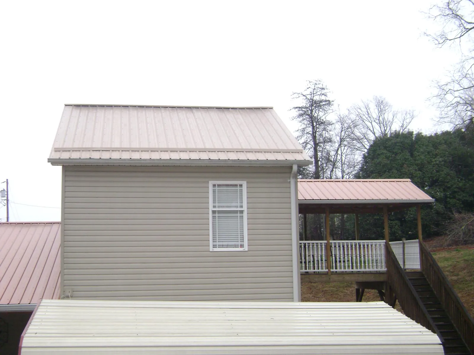 Tan metal roofs on a two story addition and attached porch, from a Roof Replacement job in Campbell Hall